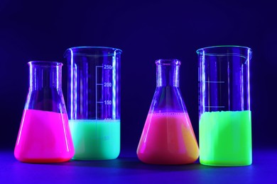 Laboratory glassware with luminous liquids on dark blue background