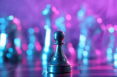 Photo of Metal pawn on chessboard in color light, selective focus