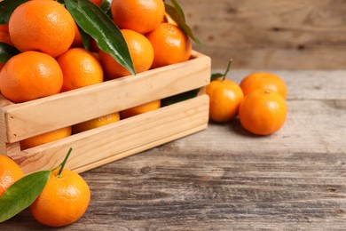 Photo of Delicious tangerines with leaves on wooden table, closeup. Space for text