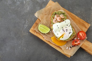 Photo of Delicious sandwich with guacamole, shrimps and fried egg on grey table, top view. Space for text