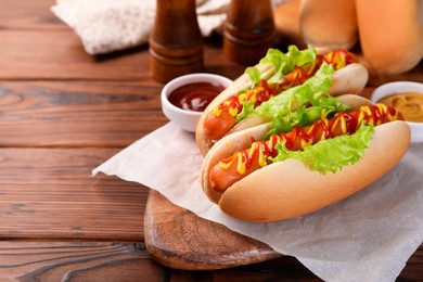 Tasty hot dogs with lettuce, ketchup and mustard on wooden table. Space for text