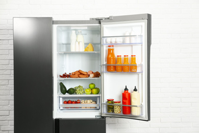 Photo of Open refrigerator filled with food near white brick wall