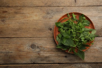 Photo of Fresh stinging nettle leaves on wooden table, top view. Space for text