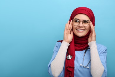 Muslim woman wearing hijab and medical uniform with stethoscope on light blue background, space for text