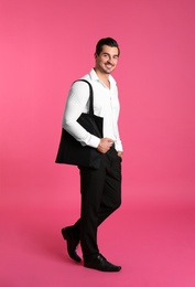 Photo of Young handsome man holding black tote bag on pink background, space for text