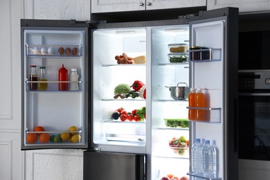 Open refrigerator full of different products in kitchen