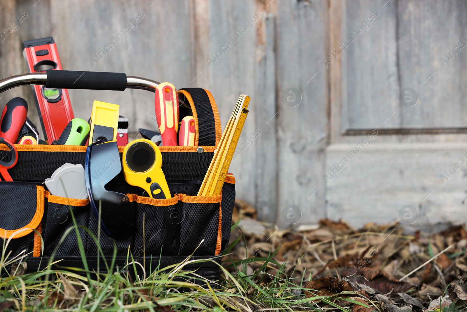 Photo of Bag with different tools for repair on grass near wooden door outdoors, space for text