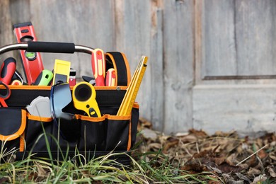 Photo of Bag with different tools for repair on grass near wooden door outdoors, space for text