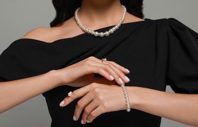Young woman wearing elegant pearl jewelry on grey background, closeup
