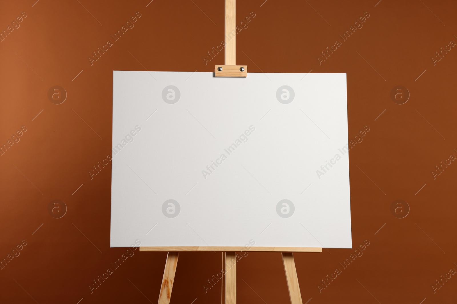 Photo of Wooden easel with blank canvas on brown background