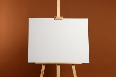 Photo of Wooden easel with blank canvas on brown background