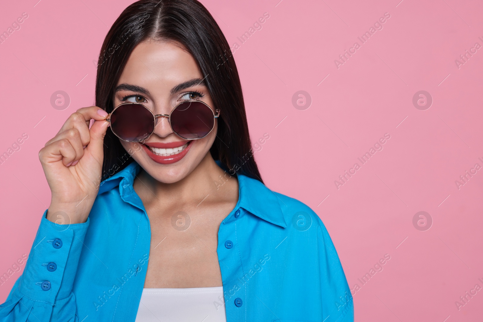 Photo of Attractive happy woman touching fashionable sunglasses against pink background, closeup. Space for text