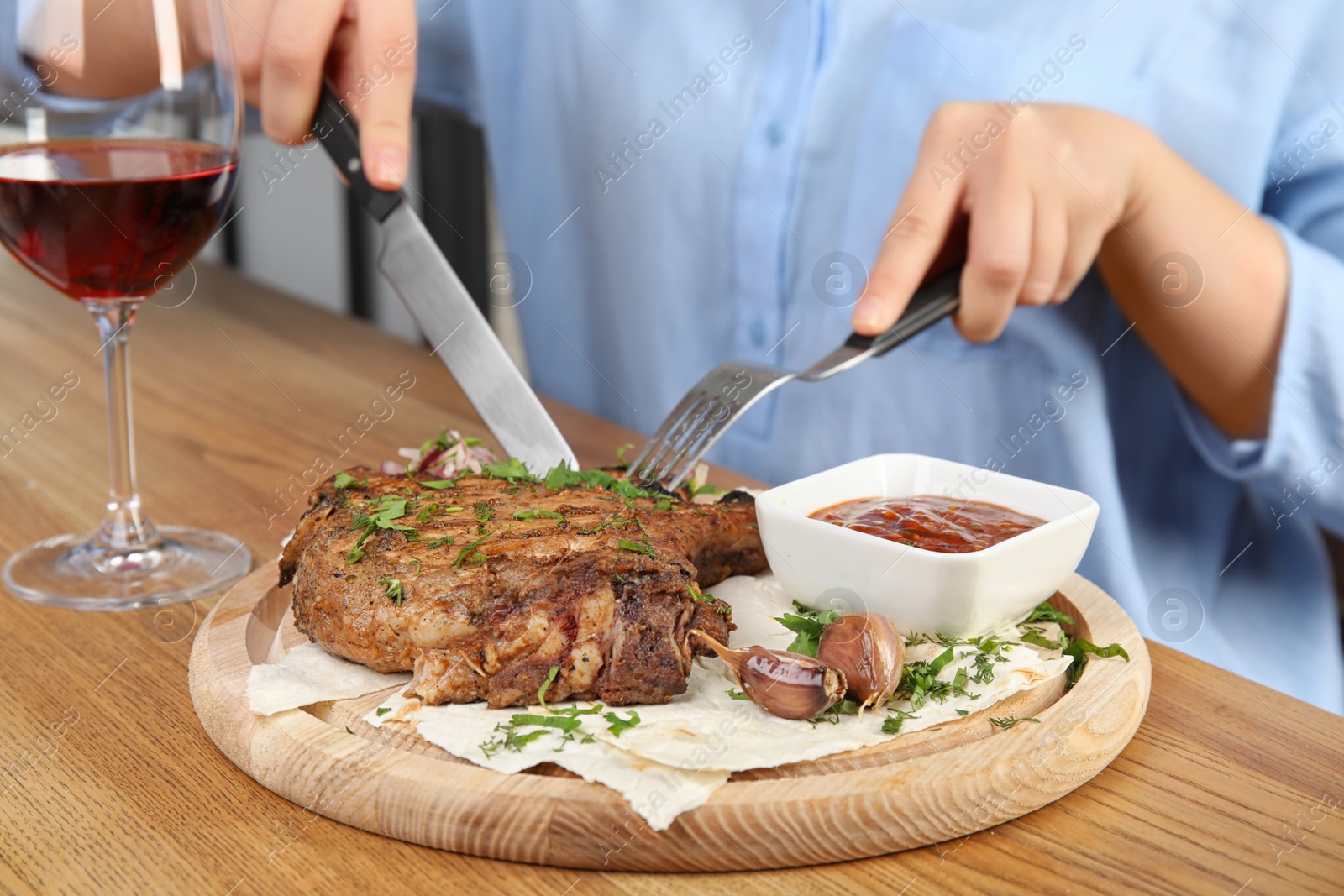 Photo of Woman eating delicious grilled pork chop at wooden table indoors, closeup