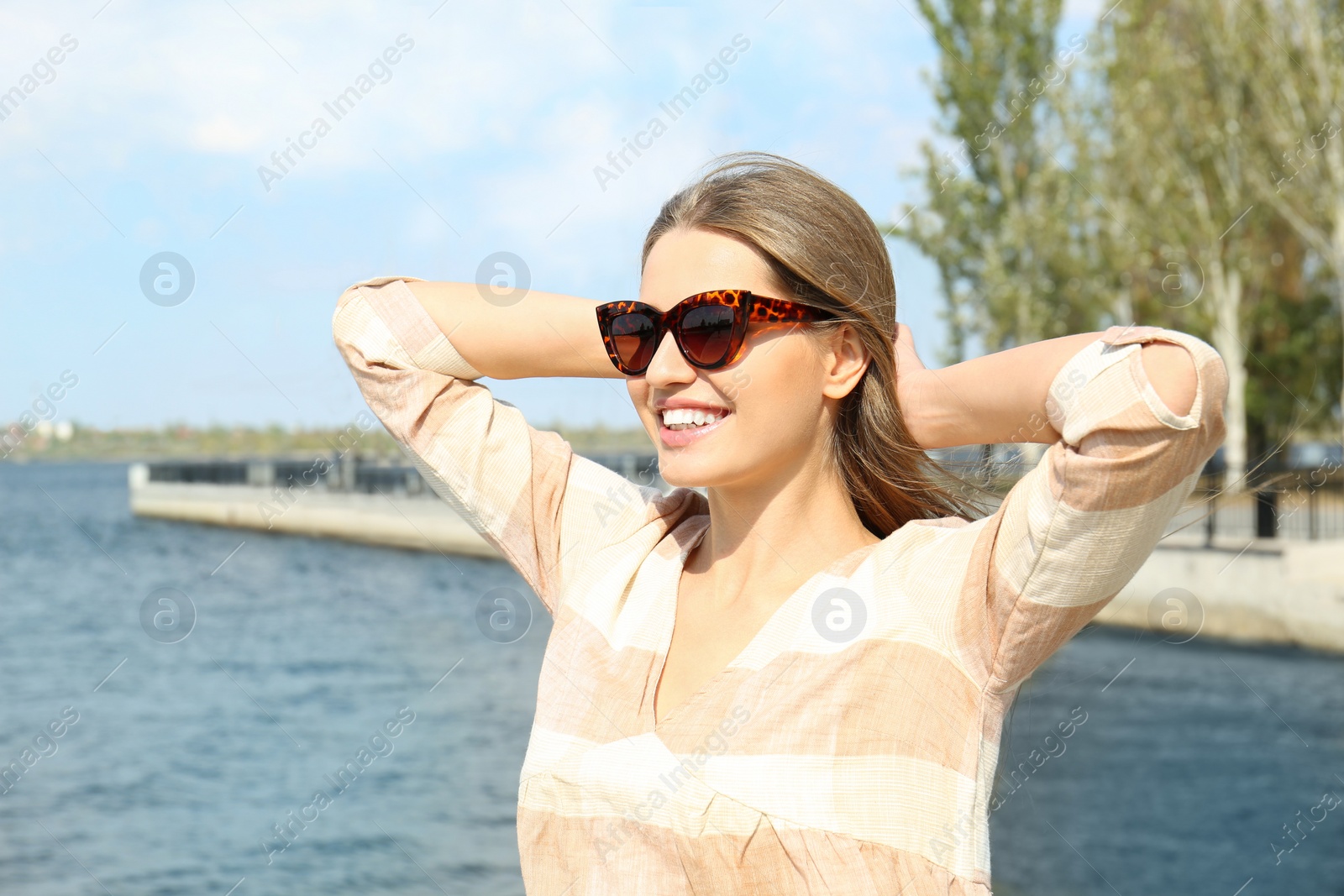 Photo of Young woman wearing stylish sunglasses near river