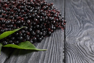 Photo of Ripe elderberries with green leaves on black wooden table, space for text