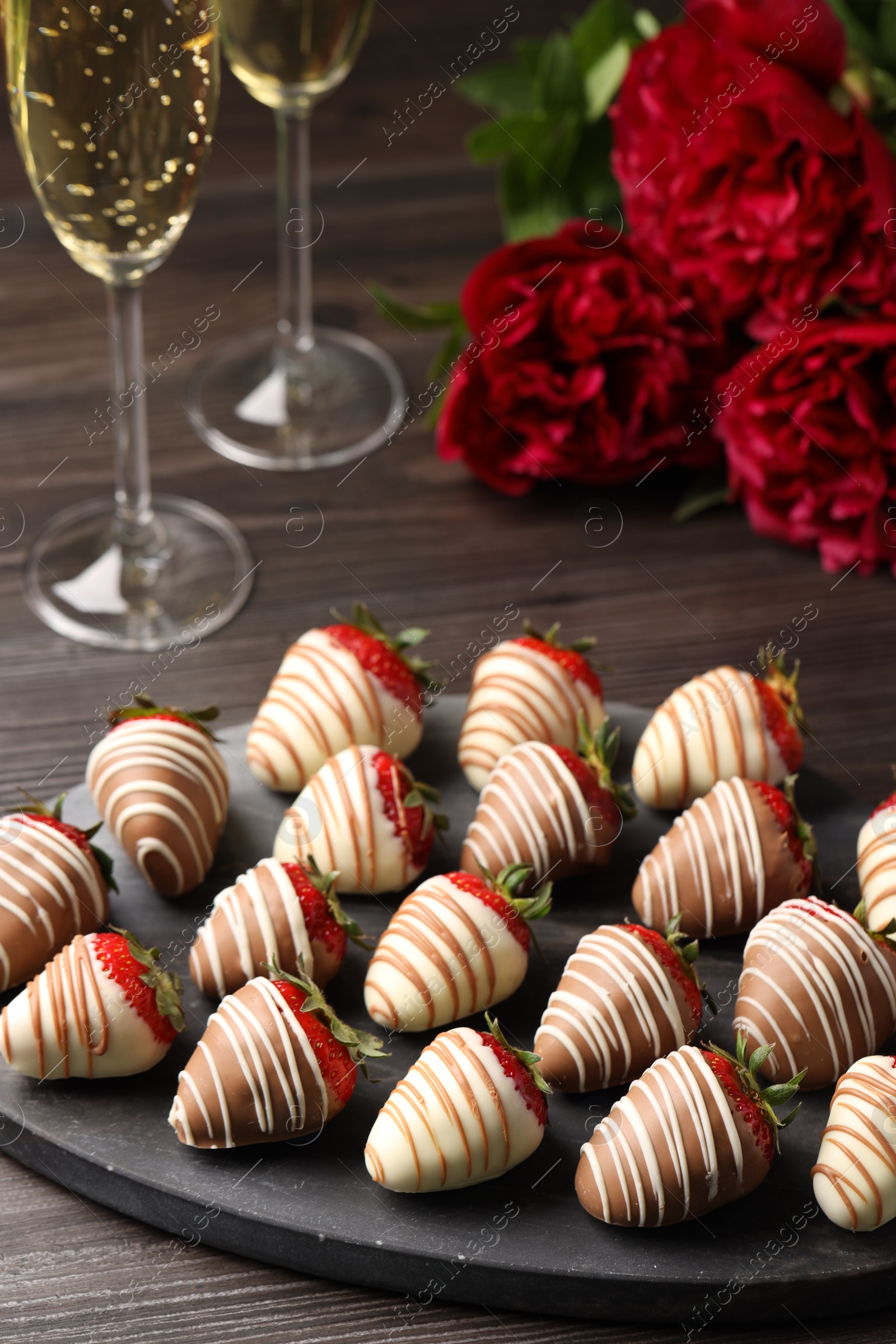 Photo of Delicious chocolate covered strawberries, sparkling wine and flowers on wooden table