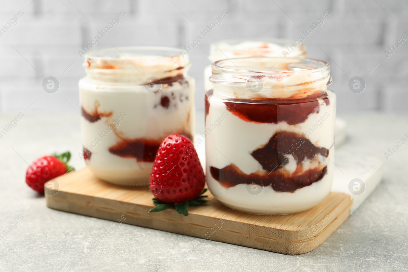 Photo of Tasty yoghurt with jam and strawberries on grey table, closeup