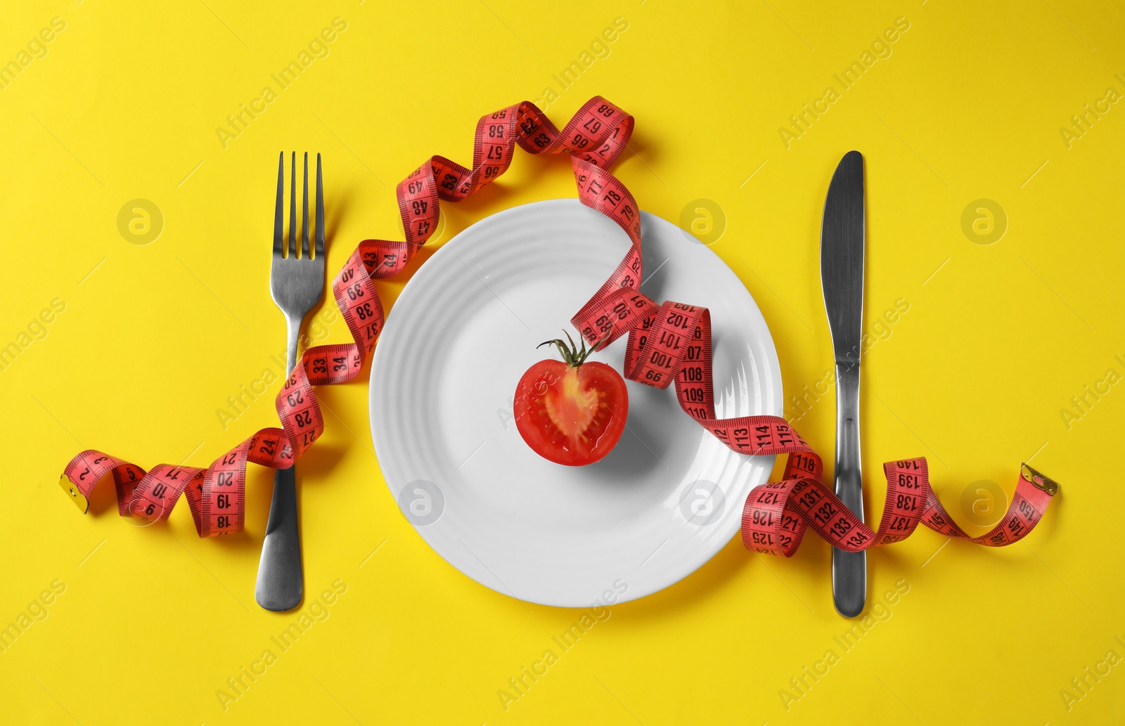 Photo of Plate with half of tomato, cutlery and measuring tape on yellow background, flat lay. Diet concept