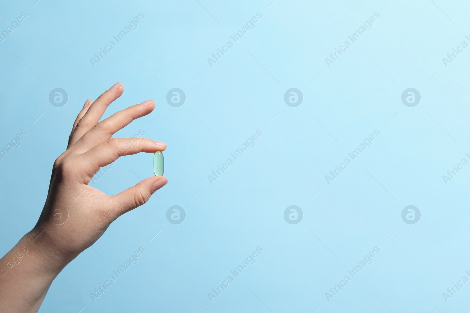 Photo of Woman holding pill on light blue background, closeup. Space for text