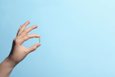 Woman holding pill on light blue background, closeup. Space for text