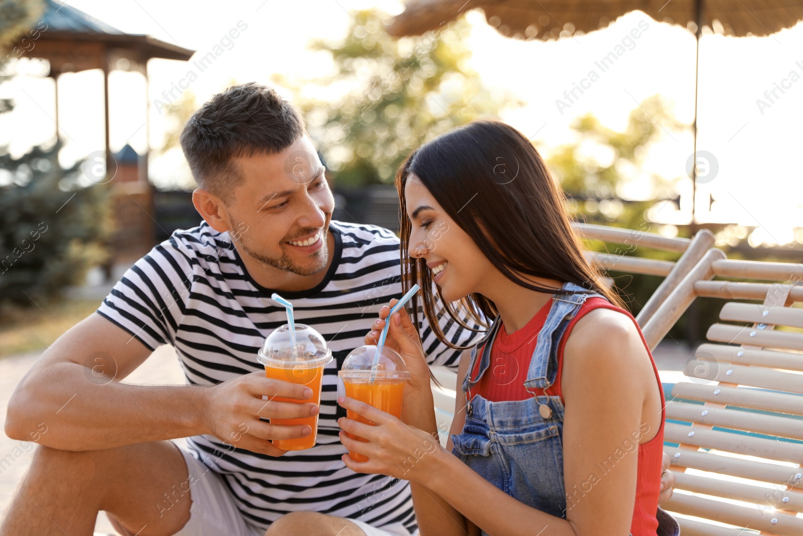 Image of Happy couple with cups of refreshing drink resting in deck chairs outdoors