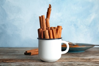 Photo of Mug with aromatic cinnamon sticks on wooden table