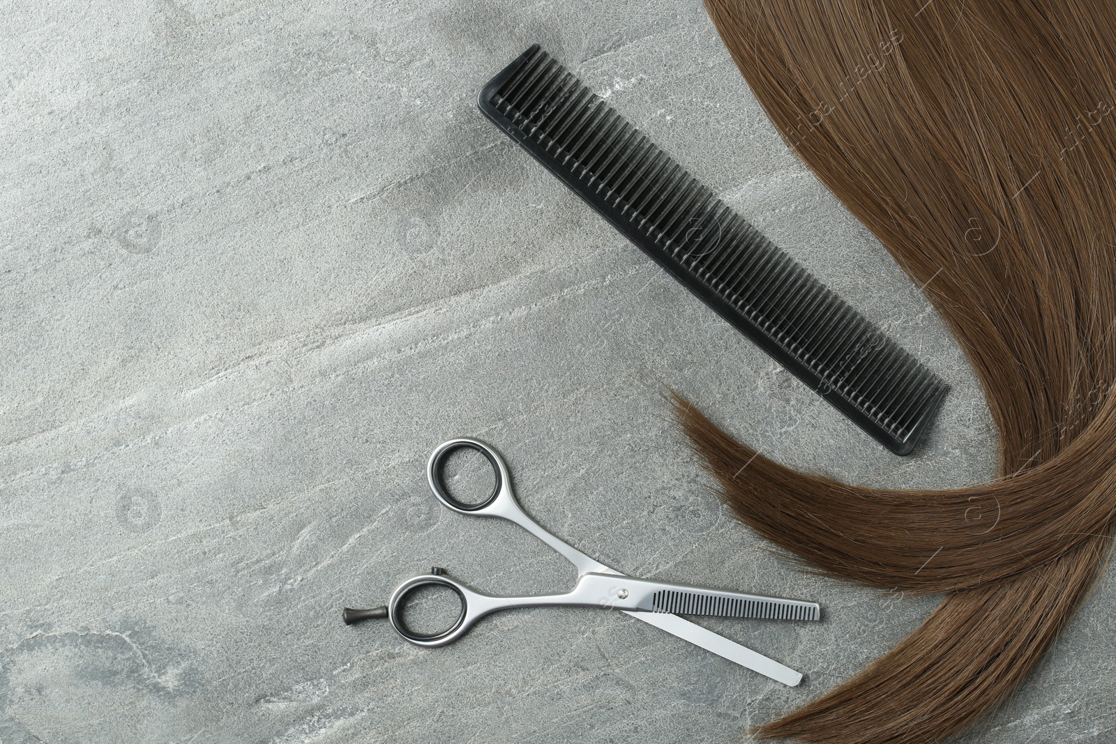 Photo of Flat lay composition with brown hair, comb, thinning scissors and space for text on grey background. Hairdresser service