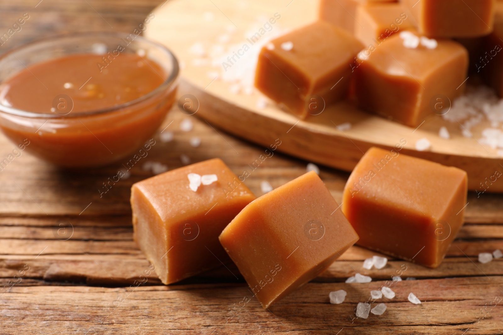 Photo of Yummy caramel candies and sea salt on wooden table, closeup