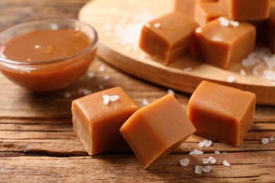 Yummy caramel candies and sea salt on wooden table, closeup