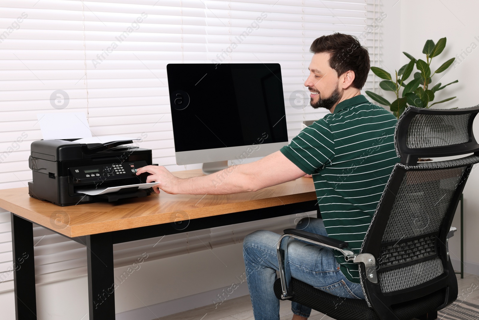 Photo of Man using modern printer at wooden table indoors