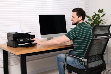 Man using modern printer at wooden table indoors