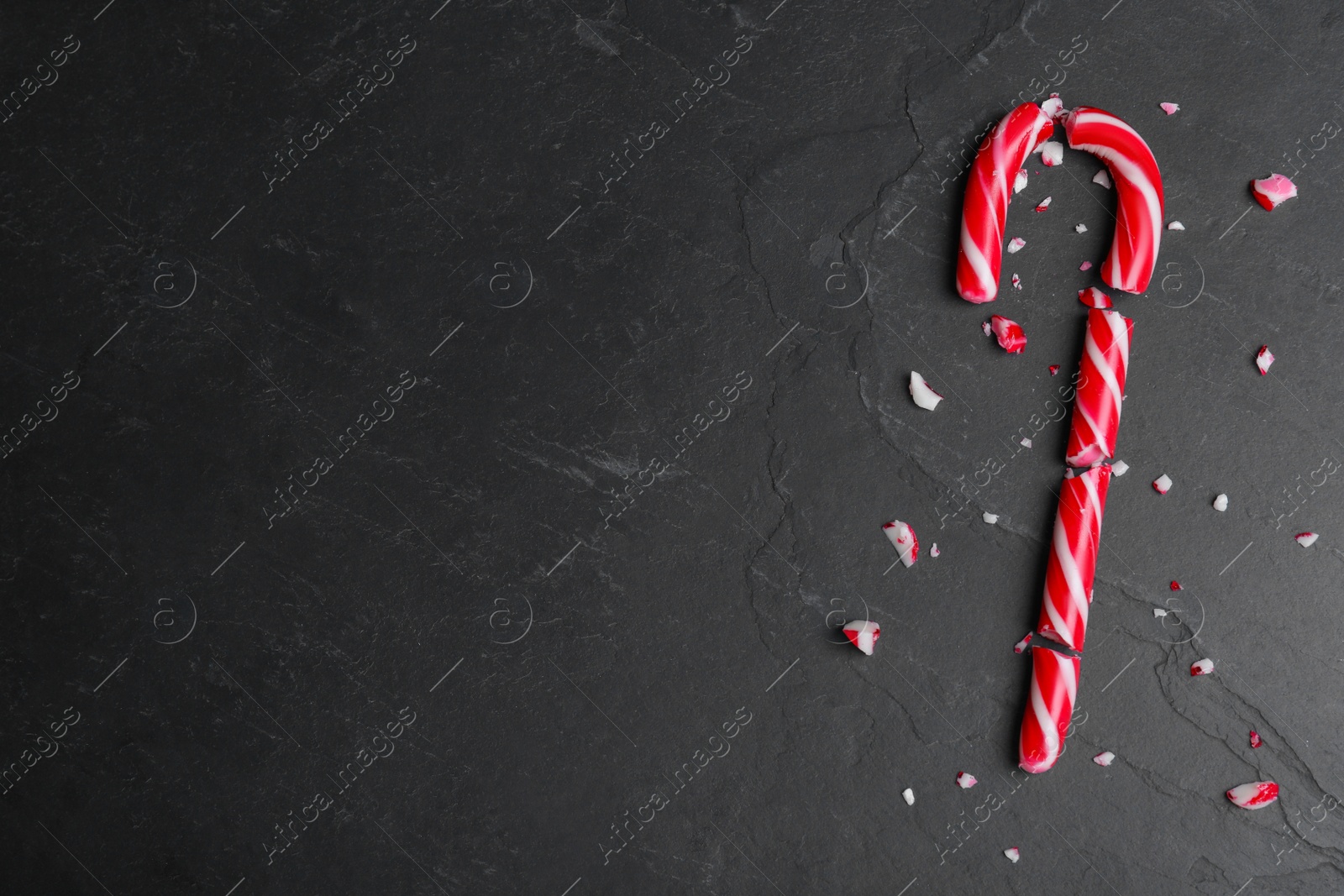 Photo of Crushed Christmas candy cane on black background, flat lay. Space for text