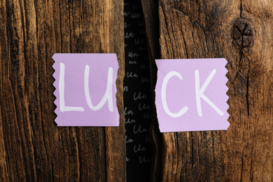 Torn card with word LUCK on wooden background