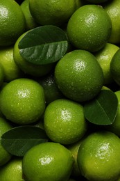 Photo of Fresh ripe limes and leaves with water drops as background, top view