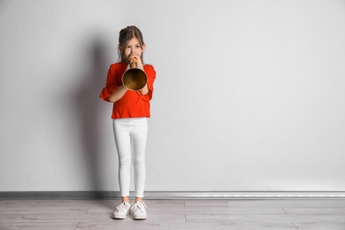 Adorable little girl with vintage megaphone near light wall