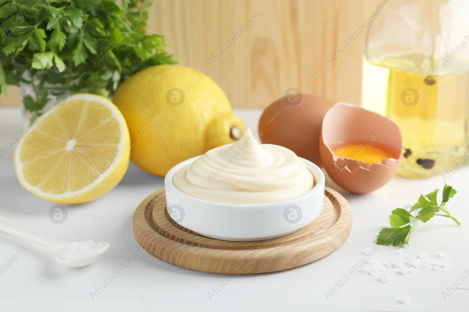 Photo of Fresh mayonnaise sauce in bowl and ingredients on white wooden table