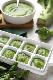 Photo of Broccoli puree in ice cube tray and ingredients on white wooden table. Ready for freezing