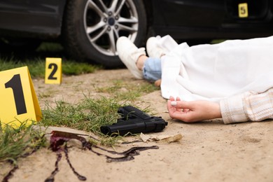 Photo of Crime scene markers, dead woman's body and gun outdoors, closeup