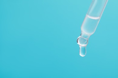 Photo of Dripping serum from pipette on light blue background, closeup. Space for text
