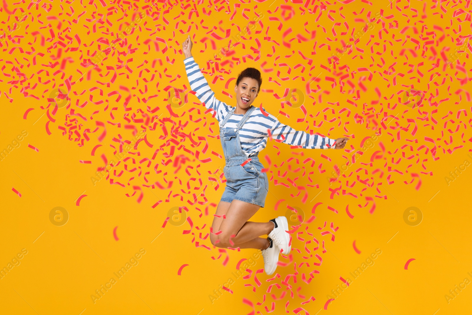 Image of Happy woman jumping in flying confetti on orange background