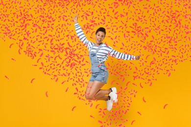 Happy woman jumping in flying confetti on orange background