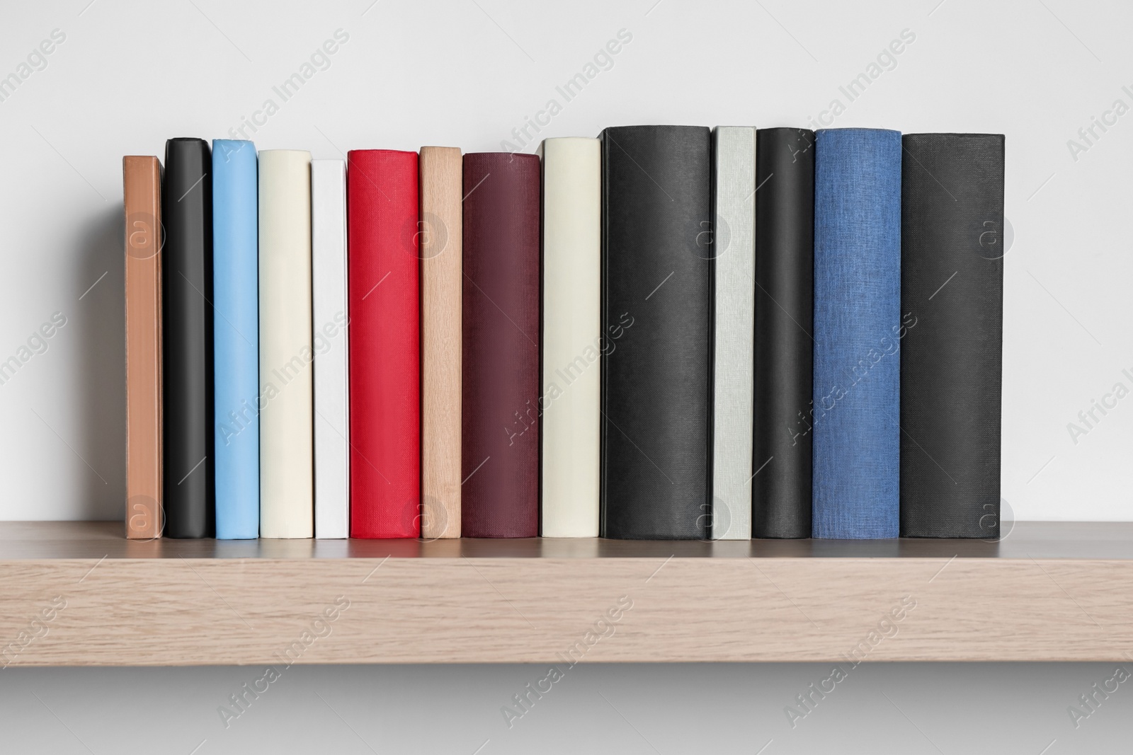 Photo of Many hardcover books on wooden shelf near white wall