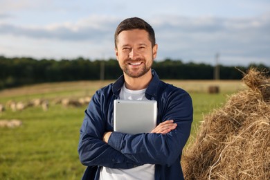Smiling farmer with tablet near hay bale on farm