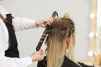 Hair styling. Hairdresser curling woman's hair in salon, closeup