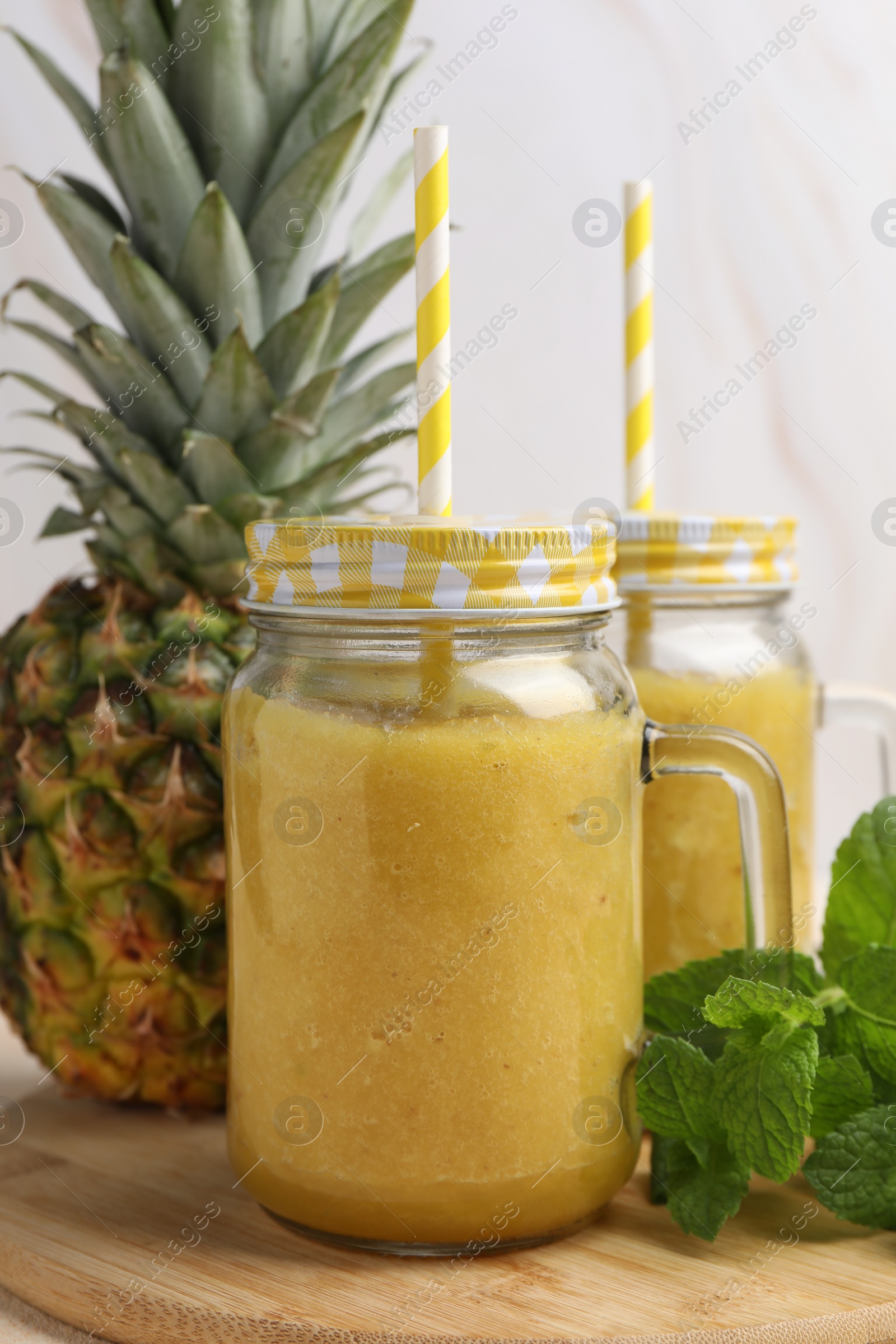 Photo of Tasty pineapple smoothie in mason jars, mint and fruit on wooden board, closeup