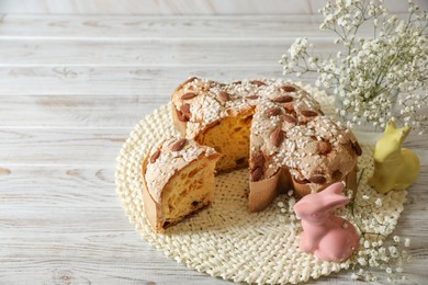 Photo of Delicious Italian Easter dove cake (traditional Colomba di Pasqua) and festive decor on white wooden table, space for text