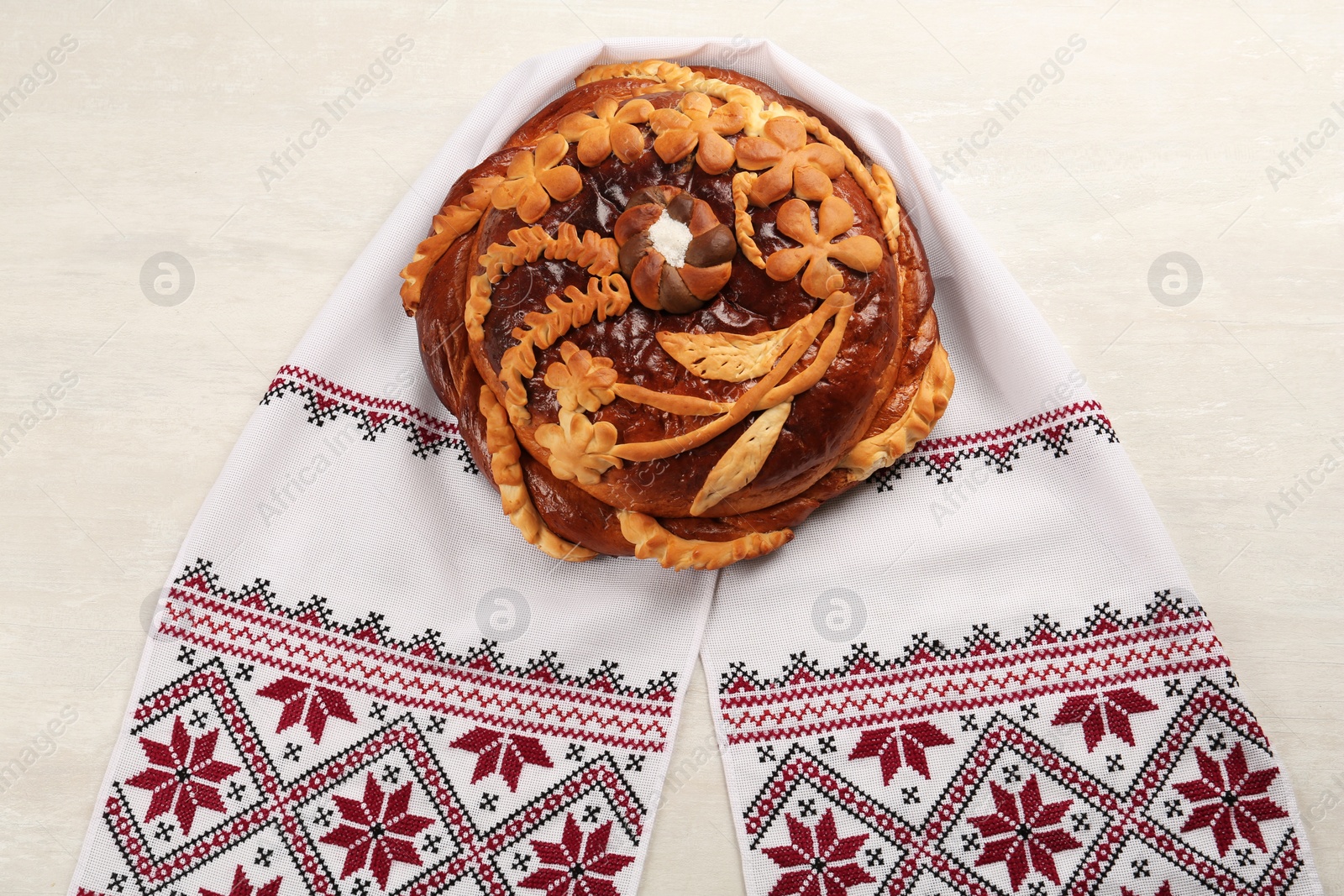 Photo of Rushnyk with korovai on white table, top view. Ukrainian bread and salt welcoming tradition