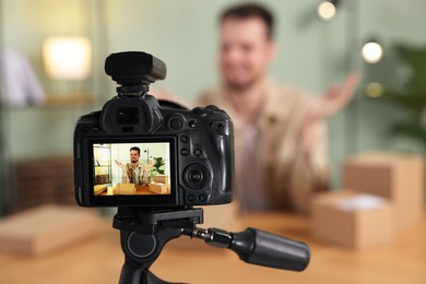 Photo of Blogger with many parcels recording video at home, focus on camera
