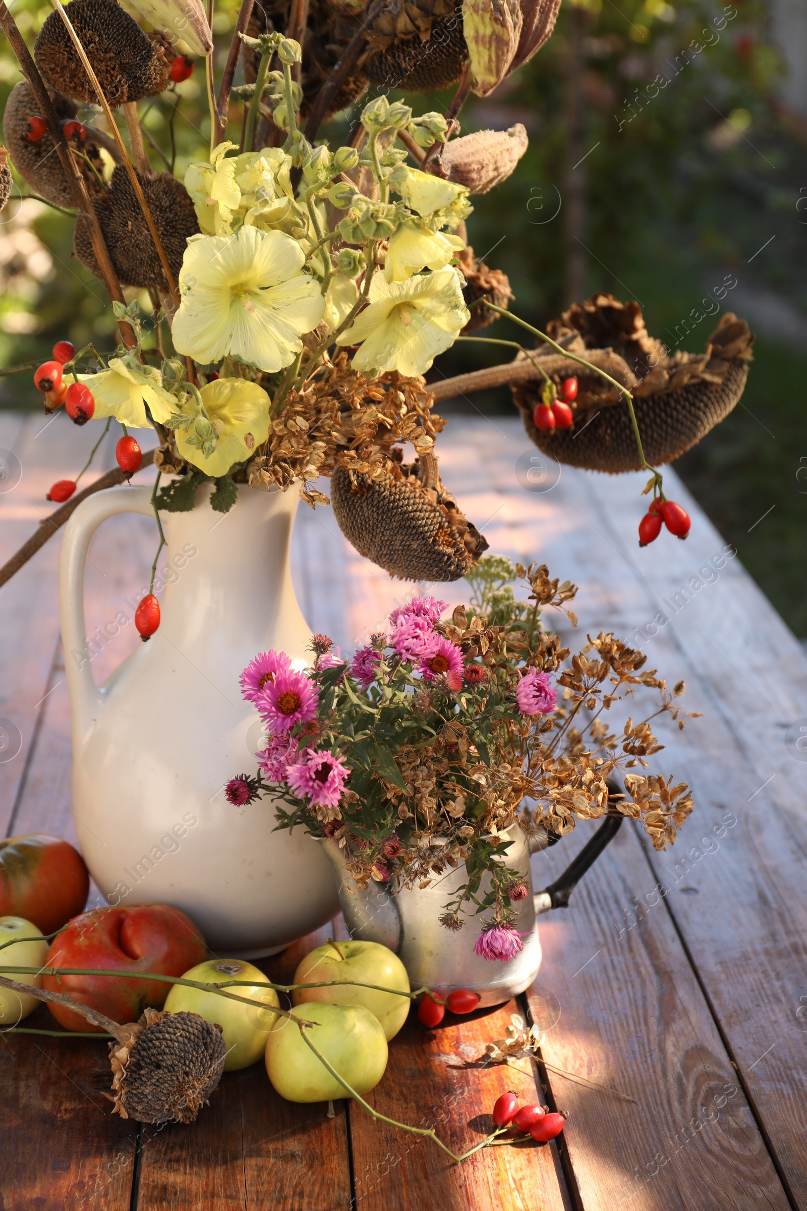 Photo of Composition with beautiful flowers, dry sunflowers and apples on wooden table outdoors. Autumn atmosphere