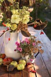 Composition with beautiful flowers, dry sunflowers and apples on wooden table outdoors. Autumn atmosphere